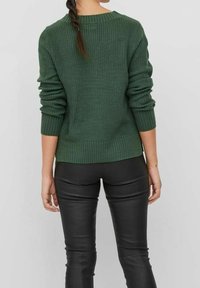 Zelený pletený svetr s žebrovanou texturou, kulatým výstřihem a dlouhými rukávy, kombinovaný s černými přiléhavými koženými kalhotami.