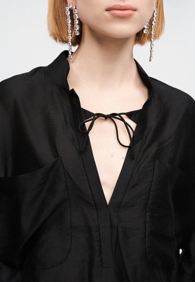 Μαύρο, ελαφρύ μπλουζάκι με V-λαιμόκοψη, δύο μπροστινές τσέπες και κλείσιμο με δέσιμο. Διαθέτει υφή υφάσματος και ελαφρώς φαρδιά μανίκια.