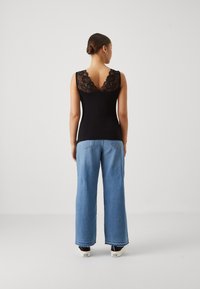Haut sans manches noir avec un dos en dentelle, associé à un jean large bleu clair et des baskets noires, vu de dos.
