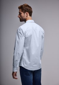 Vaaleansininen pitkähihaine paita, sileä kangas, napitus yksityiskohtia hihoissa, selän sauman ompelu, yhdistetty tummansinisiin farkkuihin. Yksinkertainen ja minimalistinen muotoilu.