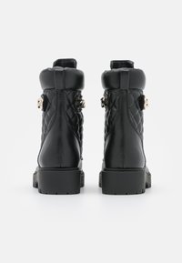 Botas de tobillo de cuero negro con diseño acolchado, punta redonda y suela de goma gruesa. Acentos de hardware dorado en los lados. Textura suave.