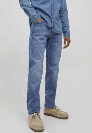 Jeans de mezclilla azul claro con corte recto, que presentan un sutil patrón de desgaste, combinados con una camisa de chambray y zapatos beige.