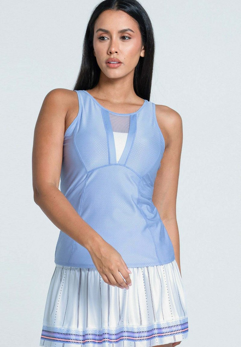 Frau mit langen dunklen Haaren, die ein ärmelloses hellblaues Oberteil mit Mesh-Detail und einen weißen plissierten Rock mit blauen Streifen trägt.