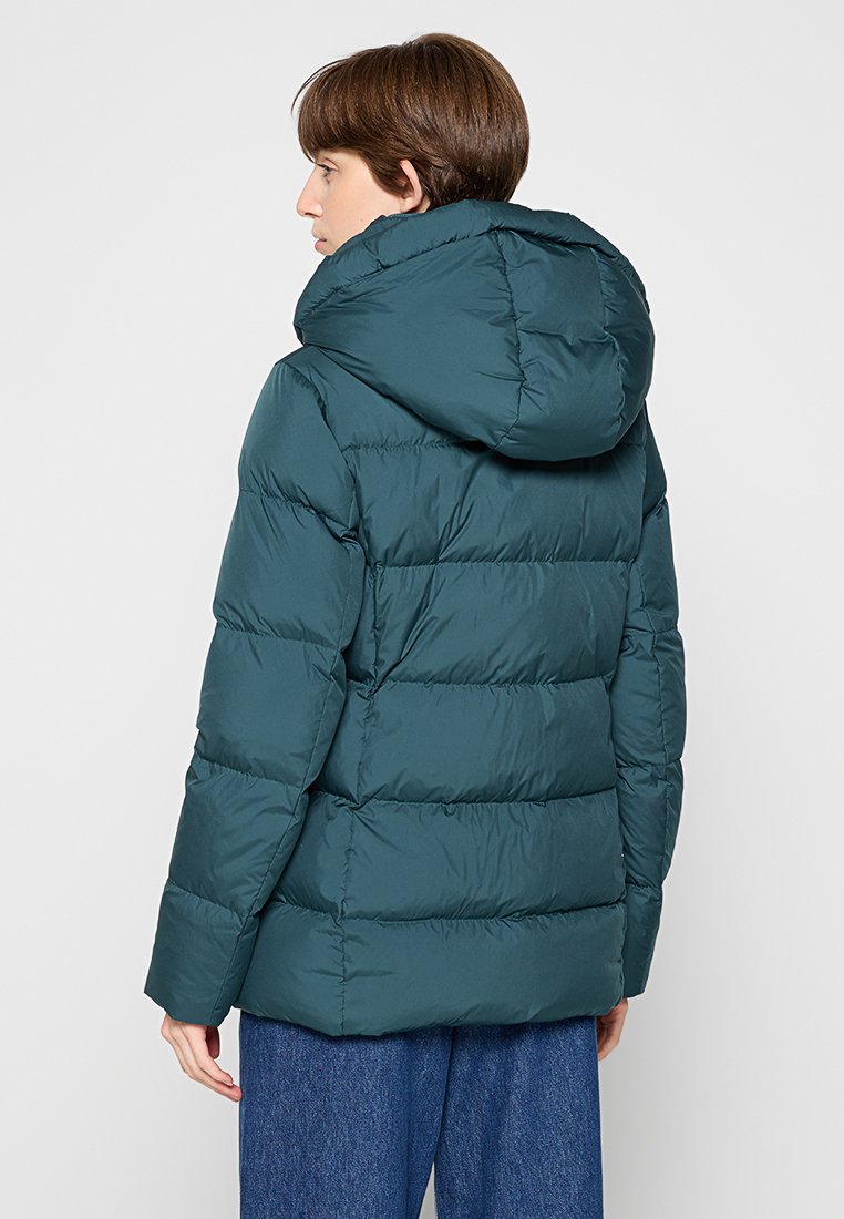 Türkiser Steppjacke mit Kapuze, die ein gesteppter Design und genähte Details aufweist. Das Material wirkt leicht und isoliert.