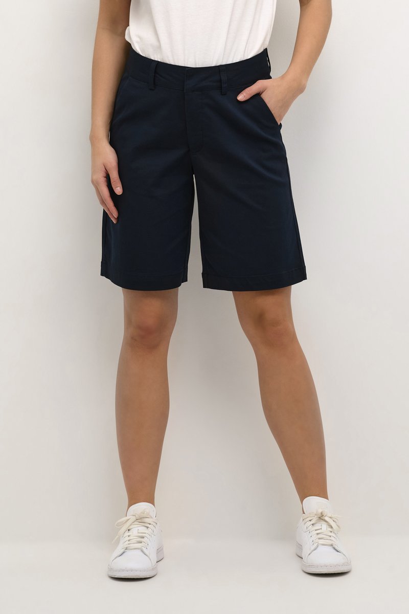 Navy blue shorts made of a flexible fabric, featuring a classic cut with side pockets and a clean hem. Paired with white sneakers.
