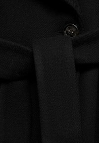 Tissu noir avec un tissage texturé, doté d'une ceinture nouée et d'un accent en bouton brillant, mettant en valeur un design épuré sans motifs visibles.