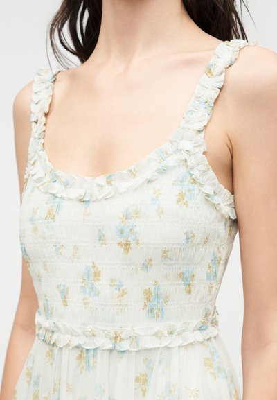 Αμάνικο λευκό φόρεμα με μπλε και μπεζ floral σχέδιο, με ραμμένο ύφασμα και βολάν στο ντεκολτέ, τα τιράντες και τη μέση.