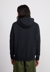 Mustapaita, joka on valmistettu pehmeästä puuvillasekoitteesta, jossa on huppu ja ribattu hihansuu. Yhdistetty löysiin oliivinvihreisiin housuihin.