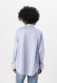 Hellblau und weiße gestreifte Button-Up-Bluse mit Rückenkonto, langen Ärmeln und entspannter Passform. Weicher Stoff mit abgerundetem Saum.