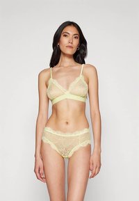 Mežģīņu bralets un tam atbilstošas biksītes pasteļdzeltenā krāsā, ar smalkiem ziedu rakstiem un regulējamām lencēm, ar mīkstu elastīgu apakšējo joslu.