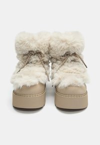 Beige műszőr csizmák vastag talppal, fémes fűzőkkel, puha textúrájú felsőrésszel és varrott részletekkel.