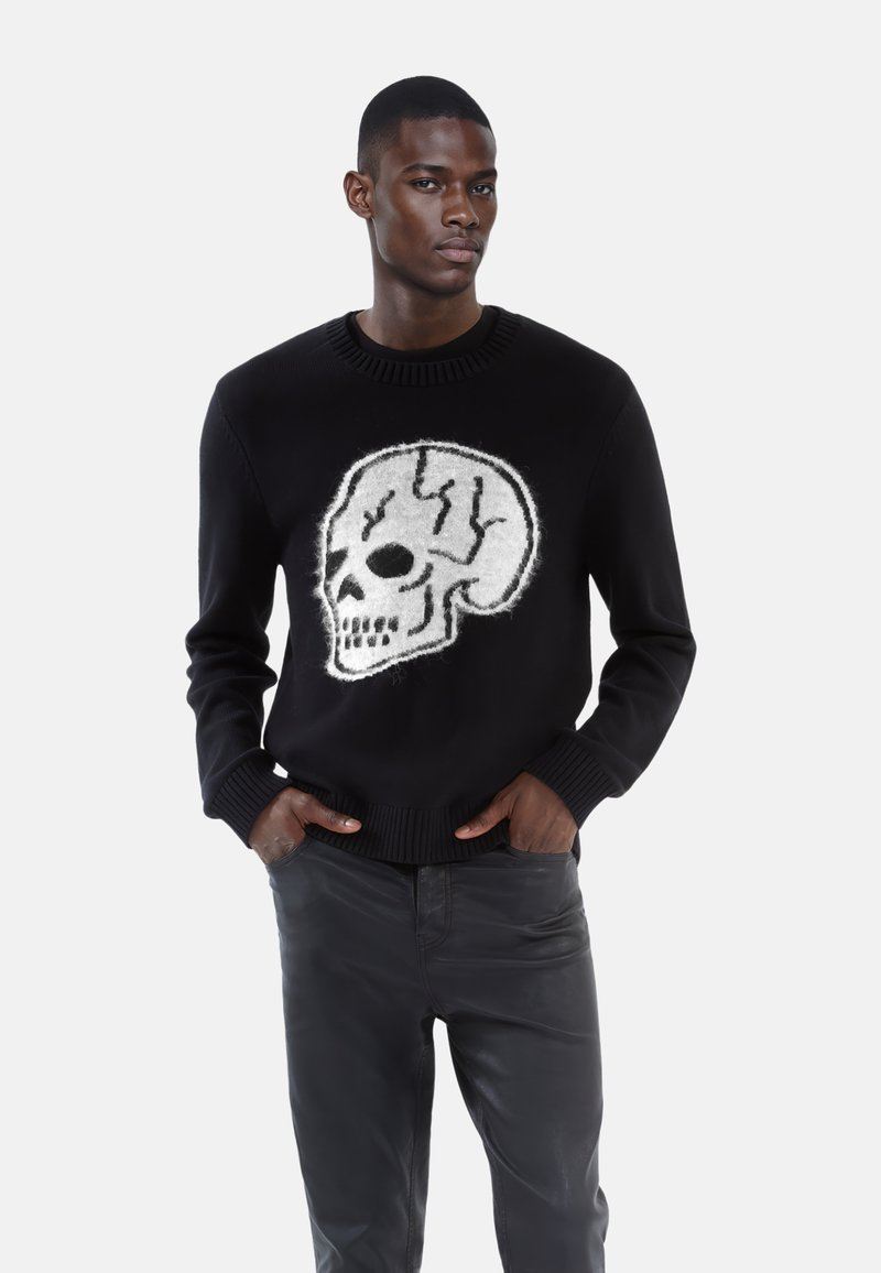 Suéter negro con un gran diseño de calavera gris en la parte frontal. Presenta un cuello y puños acanalados, combinado con pantalones oscuros.