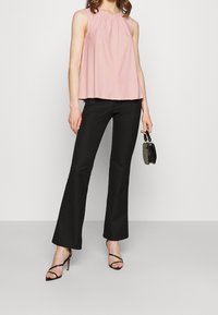 Sleeveless pink top with gathered neckline, paired with black flared trousers. The individual holds a small gray handbag and wears strappy black heels.