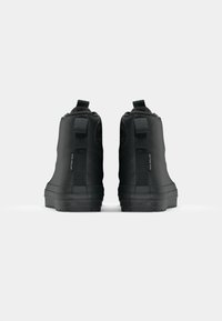 Zwarte high-top sneakers met een gestructureerde rubberen zool, versterkte hiel en trekkoordjes aan de achterkant. Kenmerkt zich door minimale branding aan de zijkant.