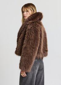 Giacca corta in pelliccia finta marrone con cappuccio, caratterizzata da una consistenza morbida e soffice e maniche ampie, abbinata a pantaloni in denim scuro.