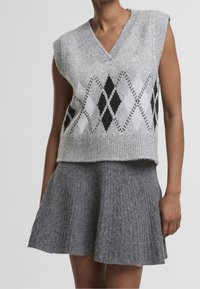 Veste sans manches en tricot gris avec motif losanges noir et blanc, associée à une jupe évasée en tricot côtelé gris portée par un mannequin.