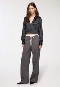 Czarna satynowa krótka koszula na guziki z luźnymi szarymi spodniami z białym sznurkiem i błyszczącymi czarnymi butami na ostro.