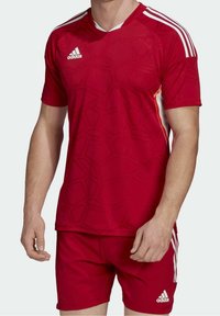 Czerwona koszulka piłkarska z teksturowanym heksagonalnym wzorem, z białymi paskami na ramionach oraz logo adidas. W zestawie z pasującymi szortami.