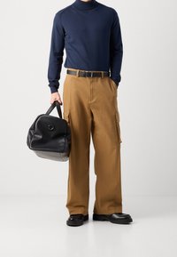 Marineblauer Rollkragenpullover, hellbraune Cargo-Hose mit Seitentaschen, schwarzer Gürtel und schwarze Ledertasche; oversized Schnitt mit glatter Textur.
