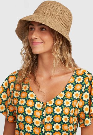 Austs ar salmiem austs bucket cepure gaiši brūnā krāsā, kopā ar kleitu ar ziedu rakstu, kurā attēloti oranži un balti ziedi uz zaļa fona.