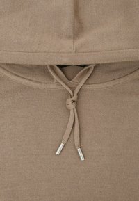 Brunt strikket hættetrøjestof med en snøre bundet i en knude og metalender på enderne.