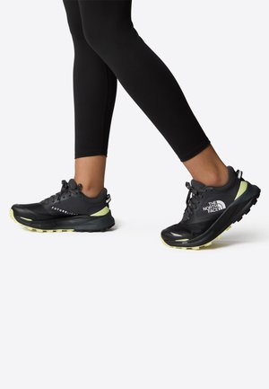 Scarpe da corsa nere con accenti gialli, tomaia in rete testurizzata, suole robuste e lacci. Il marchio sulla parte laterale presenta "The North Face."