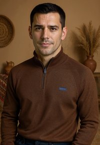 Pull zippé marron avec des accents côtelés, arborant un petit logo brodé sur la poitrine. Texture lisse, tissu léger, coupe ajustée.