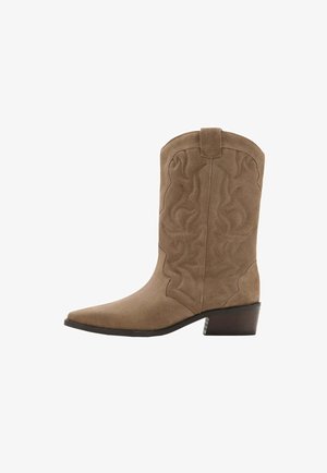 Botte de cowboy en daim beige avec bout pointu, surpiqûres décoratives, languette sur le dessus et talon bas empilé sur fond blanc.