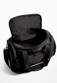 Sort duffelbag med lynlåsåbning, fremstillet af slidstærkt stof, med dobbelte håndtag og en indvendig lynlåslomme til organisering.