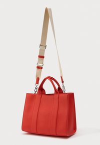 Geantă din piele texturată roșie, cu două mânere scurte și o curea de umăr bej reglabilă, pe un fundal alb.