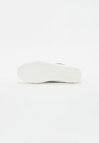Tenisky s bílou gumovou podrážkou se zubatým vzorem, hladkým černým svrškem a plochými tkaničkami pro bezpečné utažení. Minimalistický design.
