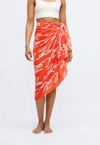 Κόκκινη ζώνη φούστας από chiffon με λευκό αφηρημένο σχέδιο, ασφαλισμένη με κορδόνι στο πλάι και διαγώνια φαρδιά άκρη για επιπλέον ροή.