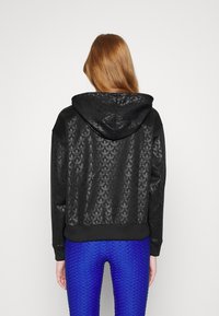 Sudadera corta negra con patrón floral texturizado, que presenta una capucha ajustable, dobladillo acanalado y mangas negras, todo sobre un fondo gris.