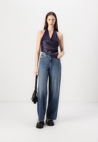 Haut à col halter violet avec un design texturé, associé à un jean en denim bleu à jambes larges avec des embellissements blancs éparpillés. Sac noir et chaussures à plateforme.
