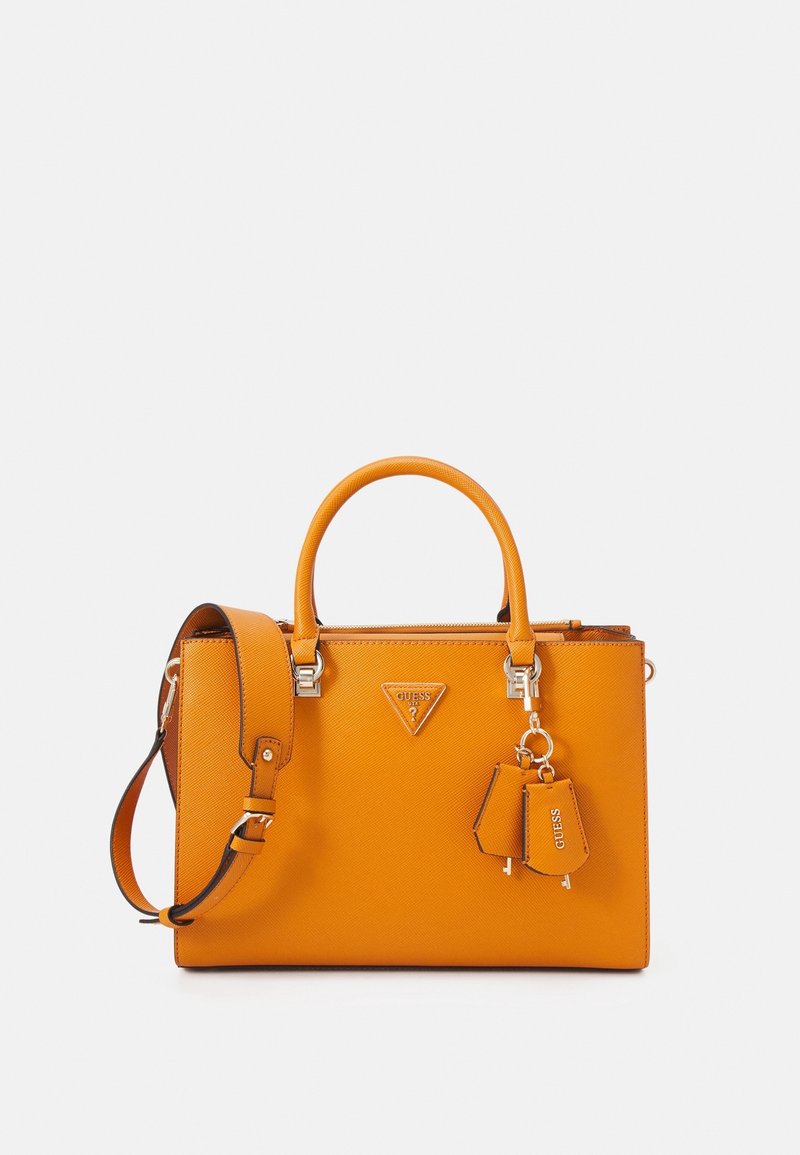 Pomarańczowa syntetyczna torebka o usztywnionym kształcie, z podwójnymi uchwytami, odpinanym paskiem na ramię i srebrnymi elementami ozdobnymi. Zawiera logo i brelok jako akcenty.