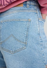 Light blue denim shorts with a high waist. Visible stitching and a single back pocket with a pointed design. Smooth texture and casual style.