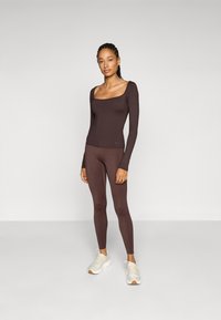 Braunes Langarmoberteil und passende Leggings aus einem glatten, dehnbaren Stoff; elegantes Design mit quadratischem Ausschnitt und nahtloser Verarbeitung.
