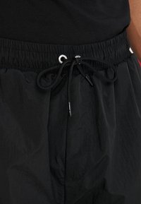 Svarta lätta joggers med elastisk midja och dragsko, metallöglor samt en slät, texturerad tygfinish.