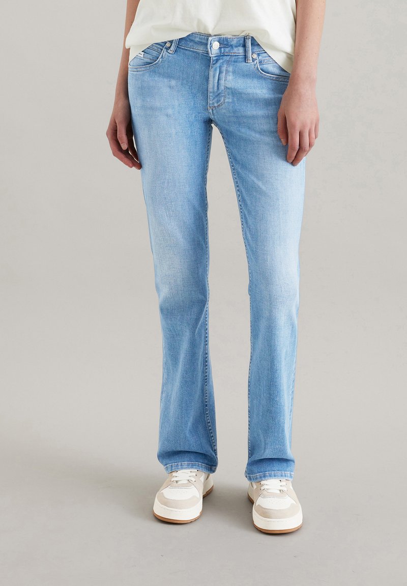 Jasnoniebieskie dżinsy o prostym kroju, pięcioma kieszeniami i zapięciem na guzik. Noszone z białymi i szarymi trampkami.