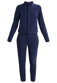 Chemise bleu marine à manches longues avec col et deux poches poitrine, associée à un pantalon slim assorti.