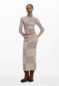 Suéter de cuello alto de punto beige acanalado y falda larga a juego con patrón de cuadros. Botas marrones de ante hasta la rodilla con cordones.