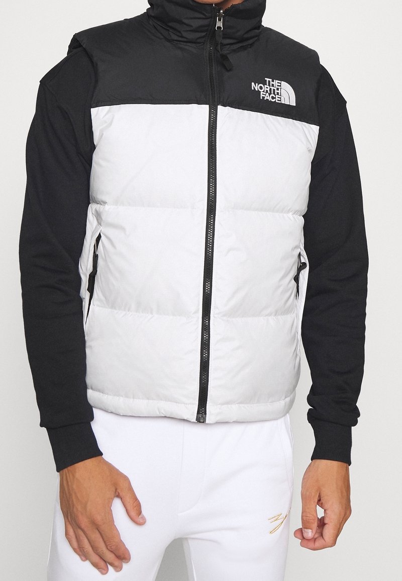 Gilet rembourré en noir et blanc, avec un col montant, une fermeture éclair à l'avant et des poches latérales. Conçu en matériau résistant aux intempéries.