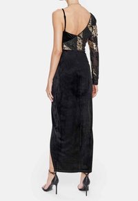 Black evening dress featuring a one-shoulder design, textured fabric, and intricate embellishments on one sleeve. High slit at the back.
