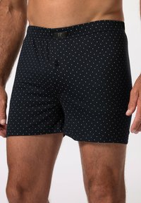 Schwarze Boxershorts aus weichem Stoff, mit einem weißen Punktmuster, elastischem Bund und einer funktionalen Frontknopf.
