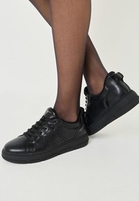 Svarta lädersneakers med rund tå, texturerad design, platt gummisula och snörning framtill. Har en greppflik vid hälen.