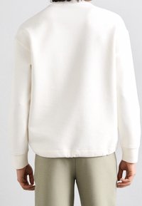 Sudadera color crema con cuello redondo, puños y dobladillo acanalados. Tejido suave, ajuste relajado y detalles de costura visibles.