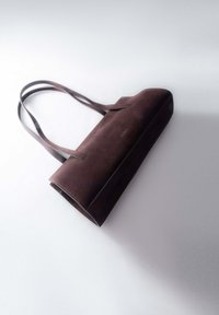 Brązowa zamszowa torba typu tote o płaskim designie, z podwójnymi uchwytami i przeszyciami. Kompaktowy kształt, gładka faktura i minimalistyczny styl.