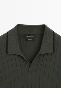 Chemise en maille côtelée vert foncé avec un col plié présentant une fine bordure noire et une étiquette Massimo Dutti à l’intérieur de l’encolure.