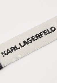 Etichetta in tessuto bianco con testo in rilievo nero "KARL LAGERFELD", caratterizzata da una superficie testurizzata e bordi cuciti.