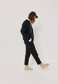 Apgriezta tumši zila džemperis ar baltu frotē odere, kombinēta ar melniem biksēm. Beigējas potīšu zābaki ar sānu rāvējslēdzēju un teksturētām zolēm.